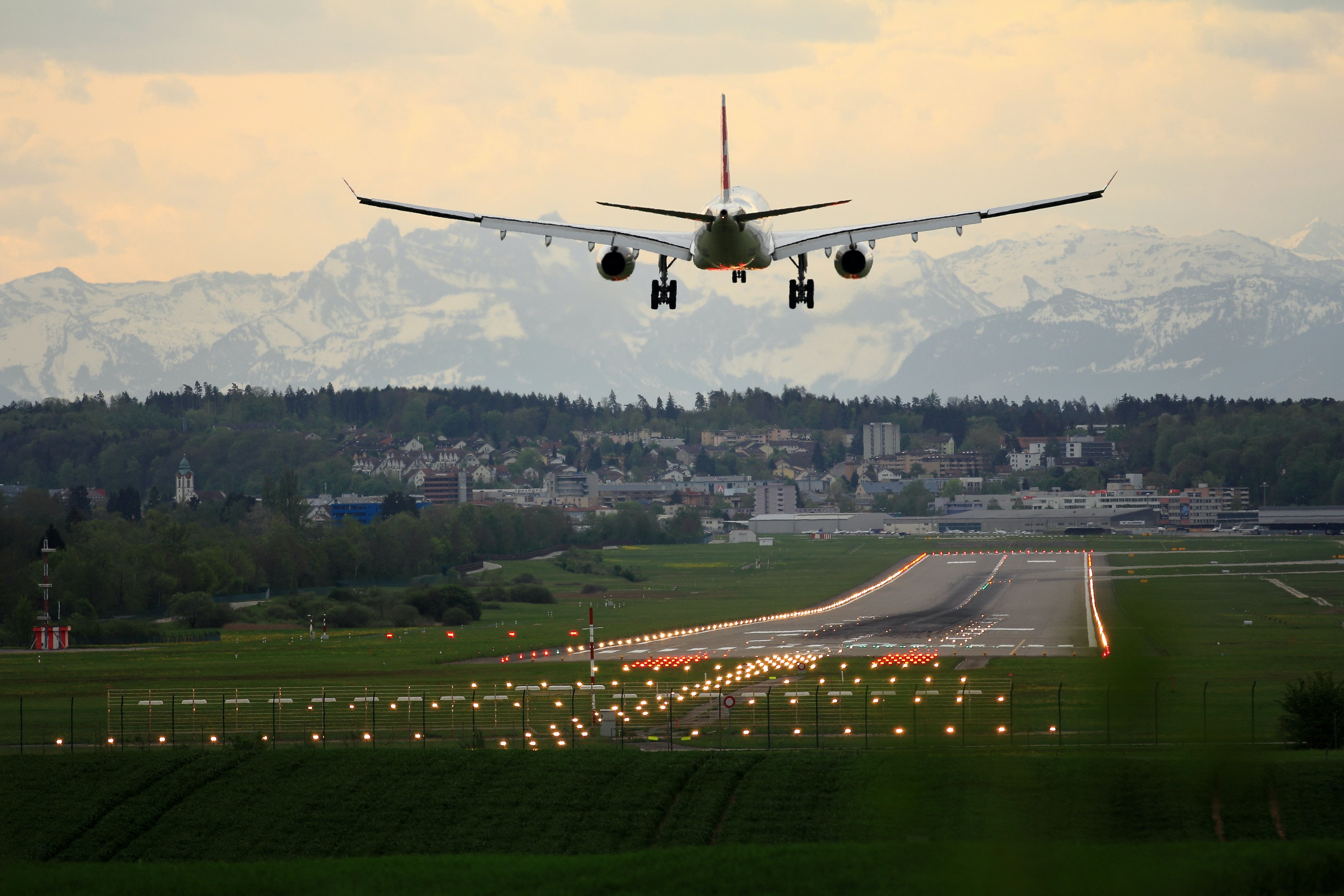 Image of an airplane coming in for a landing over a grassy landing strip with mountains in the background
