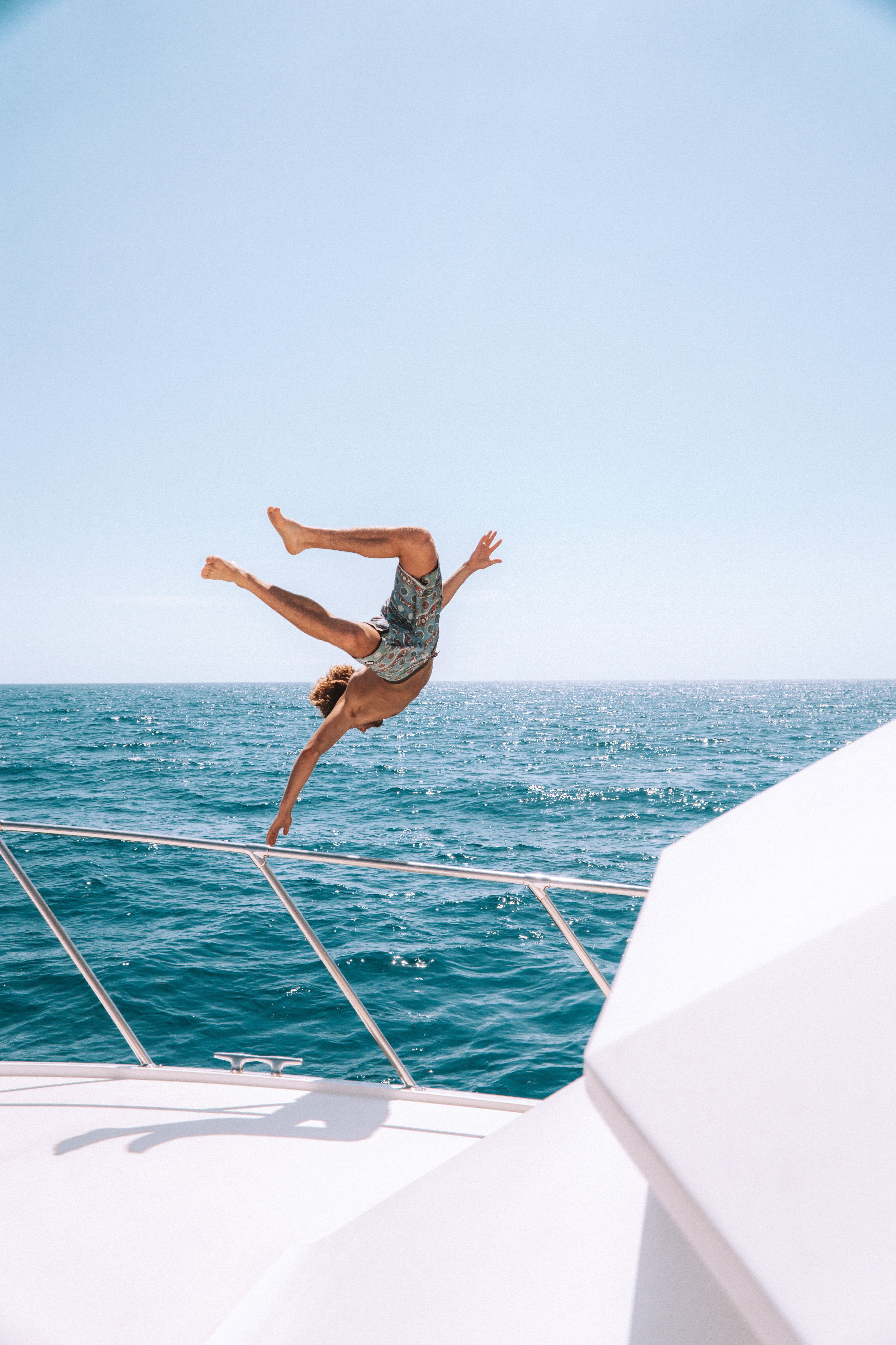Am image of a young man diving gleefully off the side of a boat in a large body of water